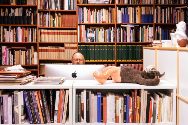 Foto av Mats Linder bak skrivebordet sitt, og foran fulle bokhyller