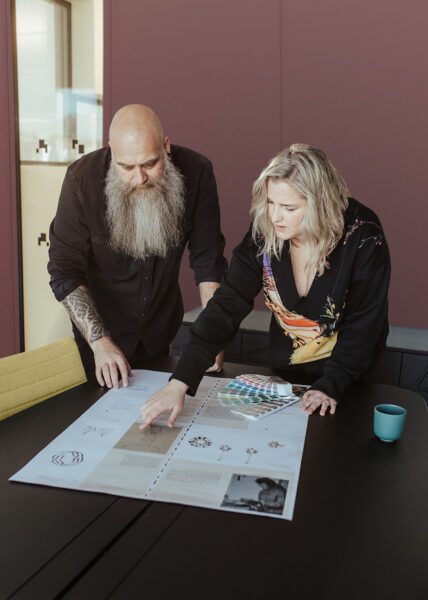Mann og kvinne står rundt et bord og diskuterer skisser som ligger på bordet